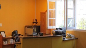 A small, yellow-toned room with a desk, chair, and a window with blinds.