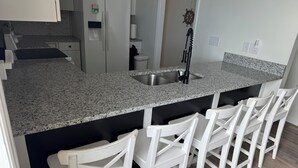 A kitchen with a granite countertop, a sink, and white bar stools. - FALL SPECIAL PRICING Beautifully Remodeled Surf City Oceanfront on the beach (Surf City)