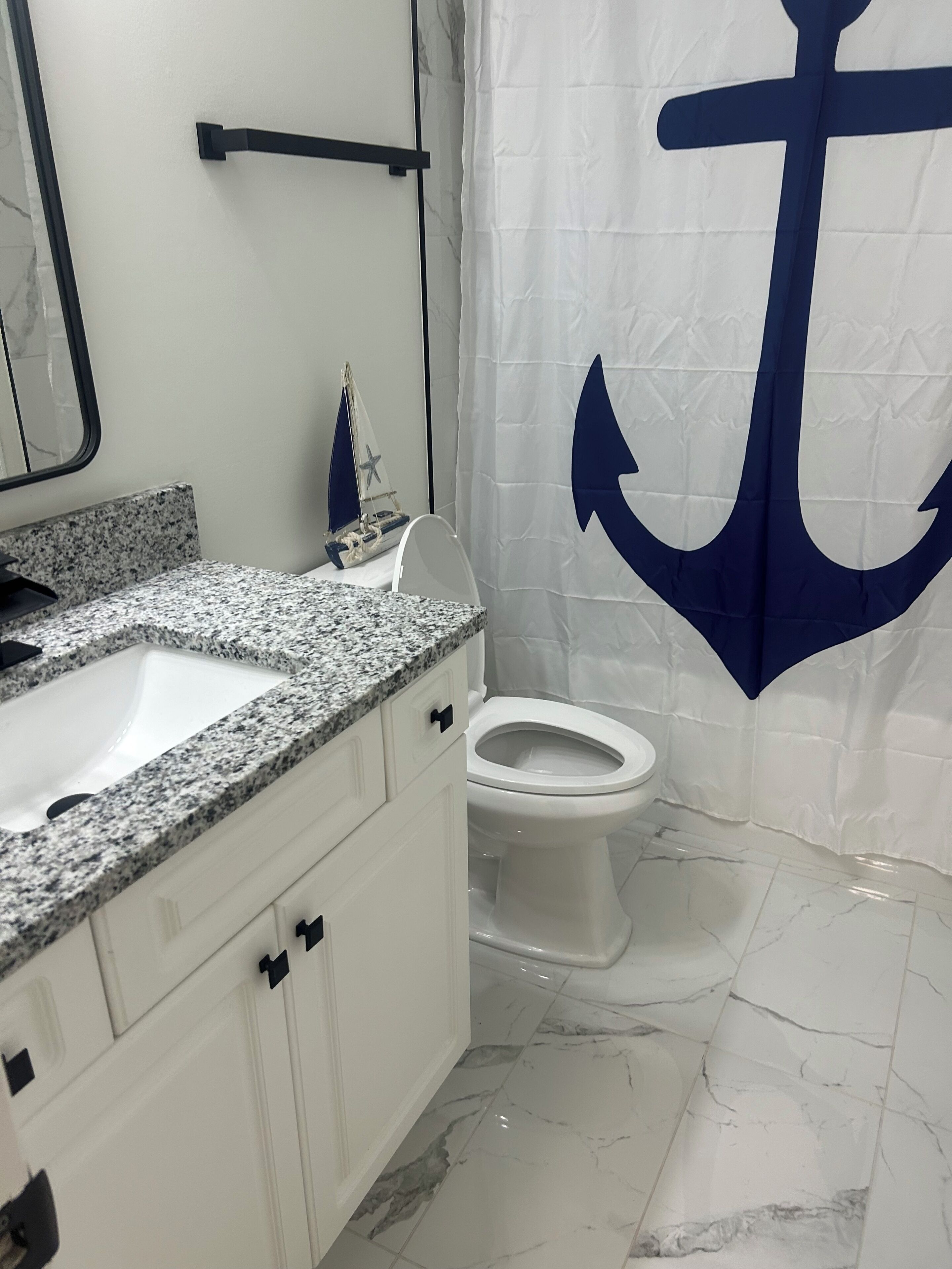 A bathroom with a white sink, a toilet, and a shower curtain with a large anchor design.