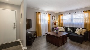 Una sala de estar con sofá, mesa de centro, televisor y ventana con cortinas.