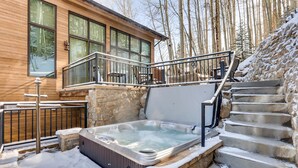Eine Holzhütte mit einer Steintreppe, die zu einem Balkon führt. Im Vordergrund ist eine Whirlpool zu sehen.