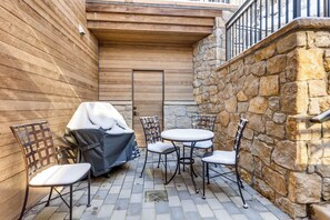 Un patio con pared de piedra, revestimiento de madera y sillas y mesas de metal.