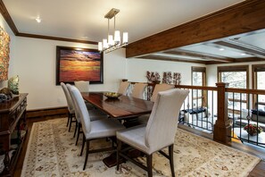 Un comedor con una mesa y sillas de madera, un candelabro, un cuadro grande y vistas a través de una barandilla de cristal.