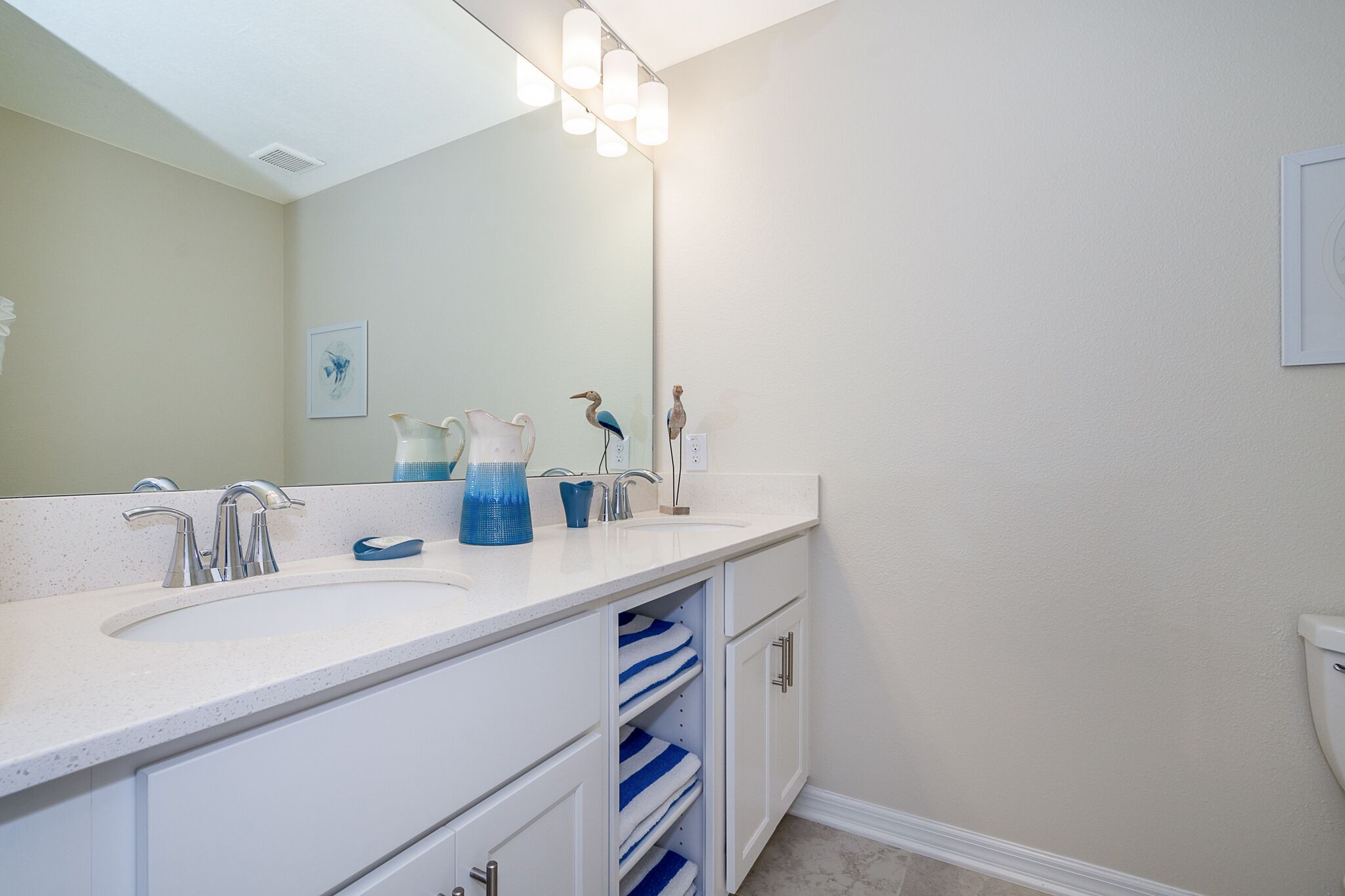 Une salle de bain avec un lavabo blanc, un miroir et un luminaire placé au-dessus.