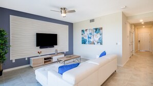 Uma sala de estar moderna com televisão de tela plana, um sofá branco, uma mesa de centro e um ventilador de teto.