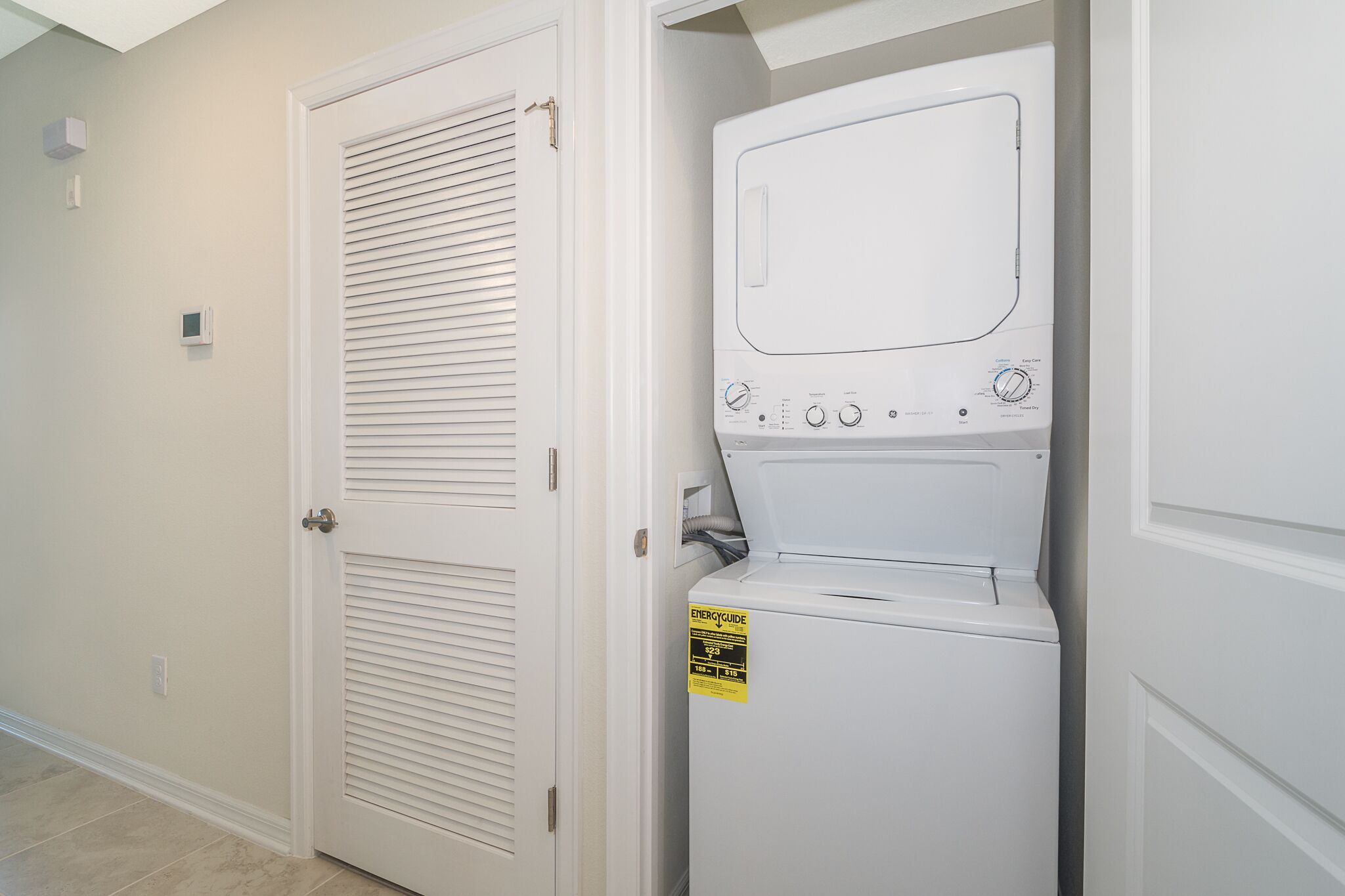 A laundry room with a front-loading washer and dryer, a door with a window, and a wall-mounted thermostat.