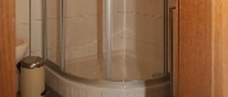 Un baño con cabina de ducha de vidrio, inodoro y cubo de basura.