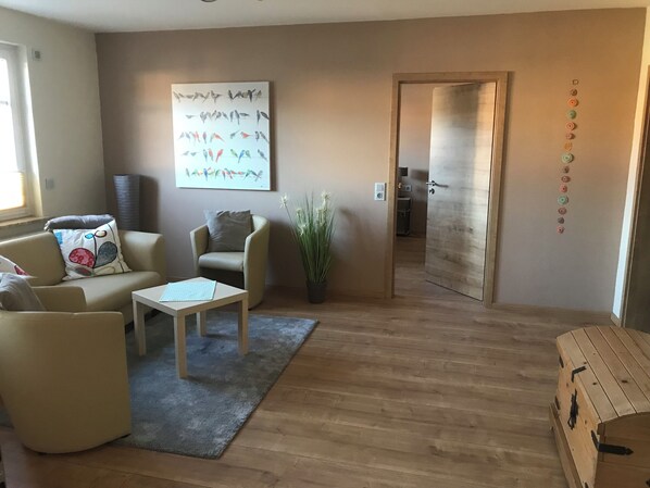 Una sala de estar con sofá, sillón, mesa de centro y un cuadro en la pared.