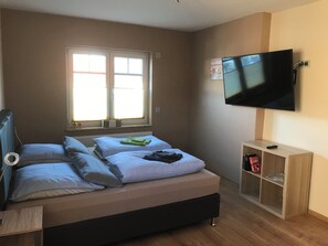 A bedroom with a bed, a TV, a window, and a small wooden cabinet. - Landhaus Beisetal (Knullwald)
