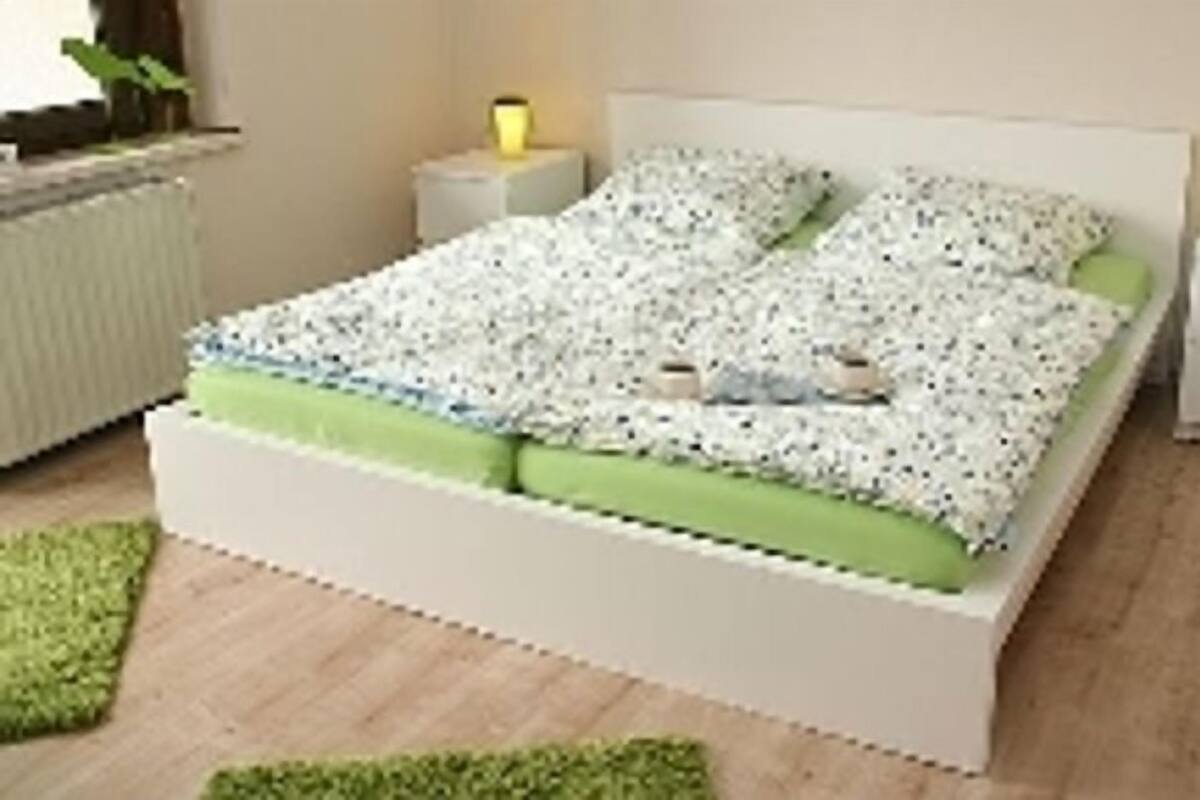 A bed with a patterned bedspread, two bedside lamps, and a green accent pillow.