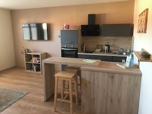 A modern kitchen with a wooden island, bar stools, a flat-screen TV, and built-in appliances. - Landhaus Beisetal (Knullwald)