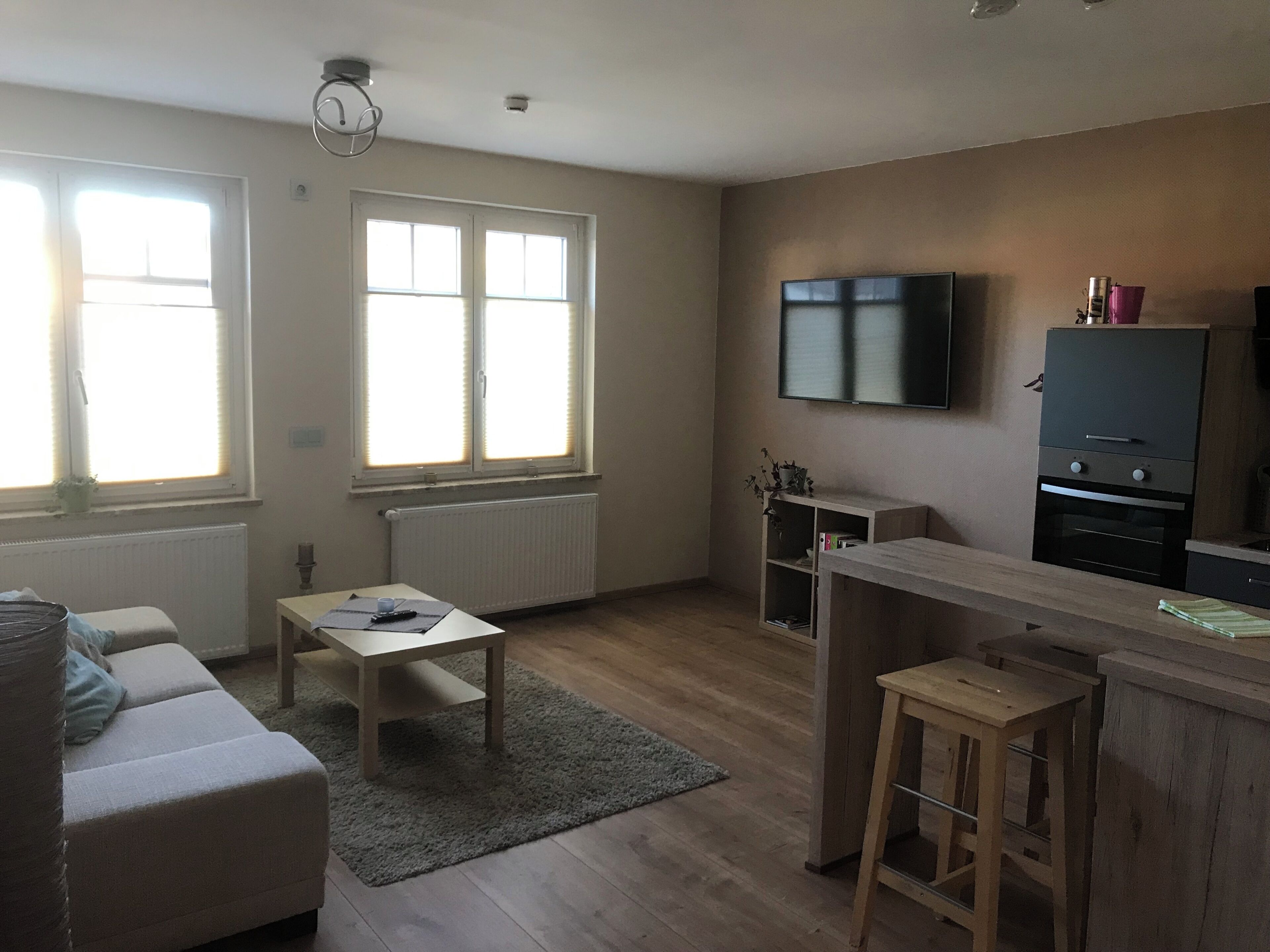 Ett vardagsrum med en soffa, ett bord, en tv och ett köksområde med kylskåp och ugn.