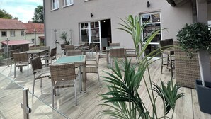 Ein Gebäude mit zahlreichen Fenstern, Außenbereich mit Sitzgelegenheiten und Pflanzkübeln.