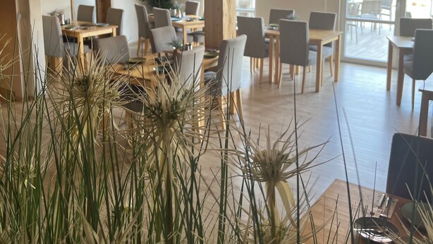 A spacious room with wooden ceilings, multiple tables and chairs, and large windows allowing natural light. - Landhaus Beisetal (Knullwald)