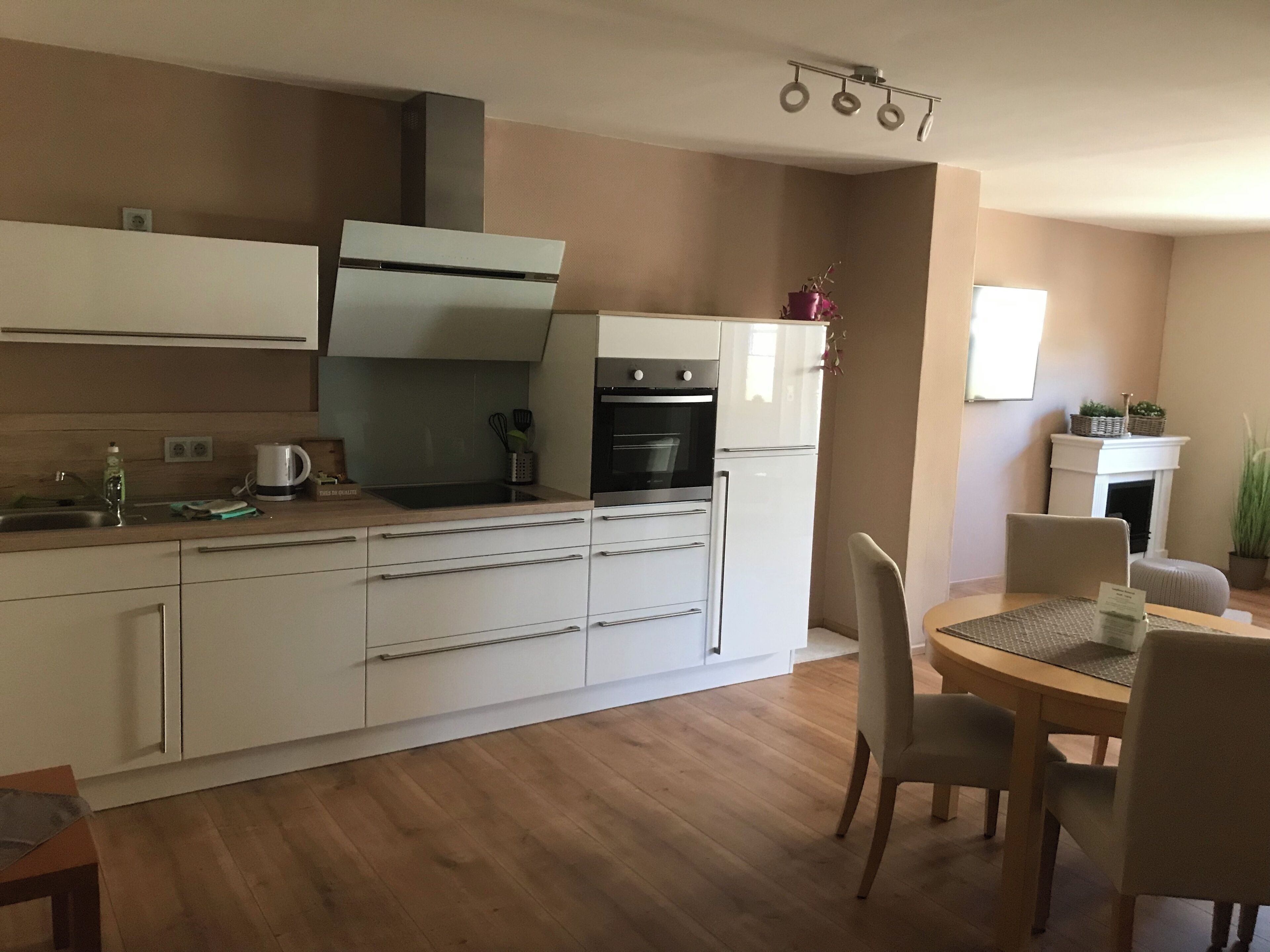 A modern kitchen with white cabinets, a built-in oven, and a dining area with a round table and chairs.