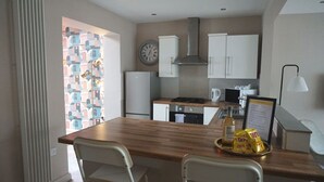A modern kitchen with white cabinets, a wooden countertop, and a view of colorful buildings through a window. - The Village House (Belfast)
