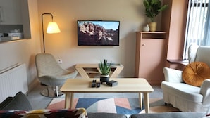 A modern living room with a sofa, armchair, coffee table, and a television mounted on the wall. - The Village House (Belfast)