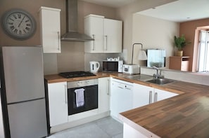 A modern kitchen with white cabinetry, a built-in oven, a microwave, a coffee maker, and a sink. - The Village House (Belfast)
