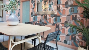 A dining area with a round table, black chairs, a vase with greenery, and a patterned wall with a mirror. - The Village House (Belfast)