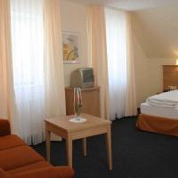 Habitación de hotel con cama, una mesita con lámpara, televisión y ventana con cortinas.