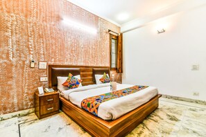 Una cama bien hecha con cabecera de madera, una mesita de noche con un teléfono y una lámpara, y una pared con diseño.