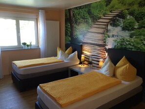 Une chambre d’hôtel avec deux lits, une fenêtre avec des rideaux, une fresque murale et des lampes de chevet.