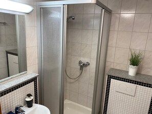 A bathroom with a glass-enclosed shower, a white bathtub, a sink with a black soap dispenser, and a potted plant on the countertop.