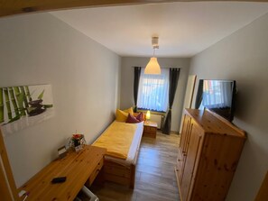 A compact room with a bed, a desk, a television, and a window with curtains.
