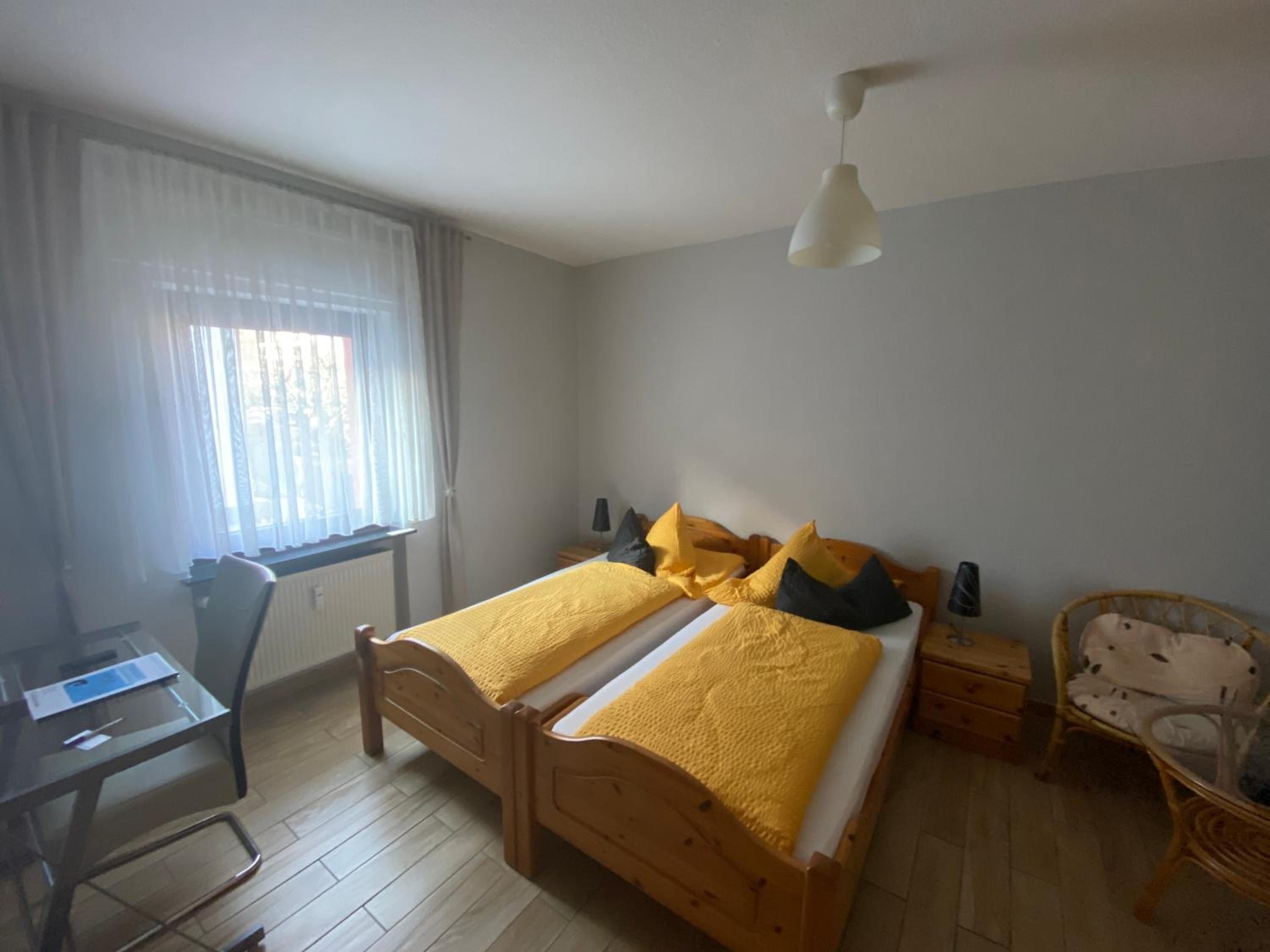 A bedroom with a wooden bed, a desk, a chair, and a window with curtains.