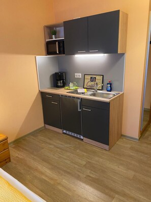 A compact kitchenette with a coffee maker, a sink, and a small shelf.