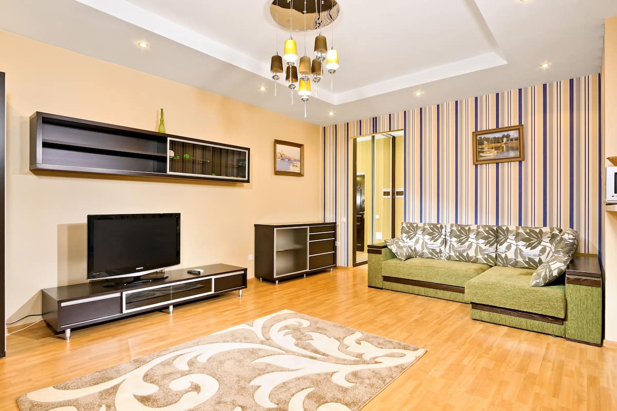 A modern living room with a flat-screen TV, a sofa, a coffee table, and a patterned rug.