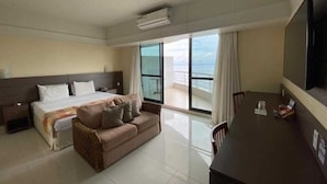 Una habitación de hotel con cama, sofá, escritorio y un amplio ventanal con vista al mar.