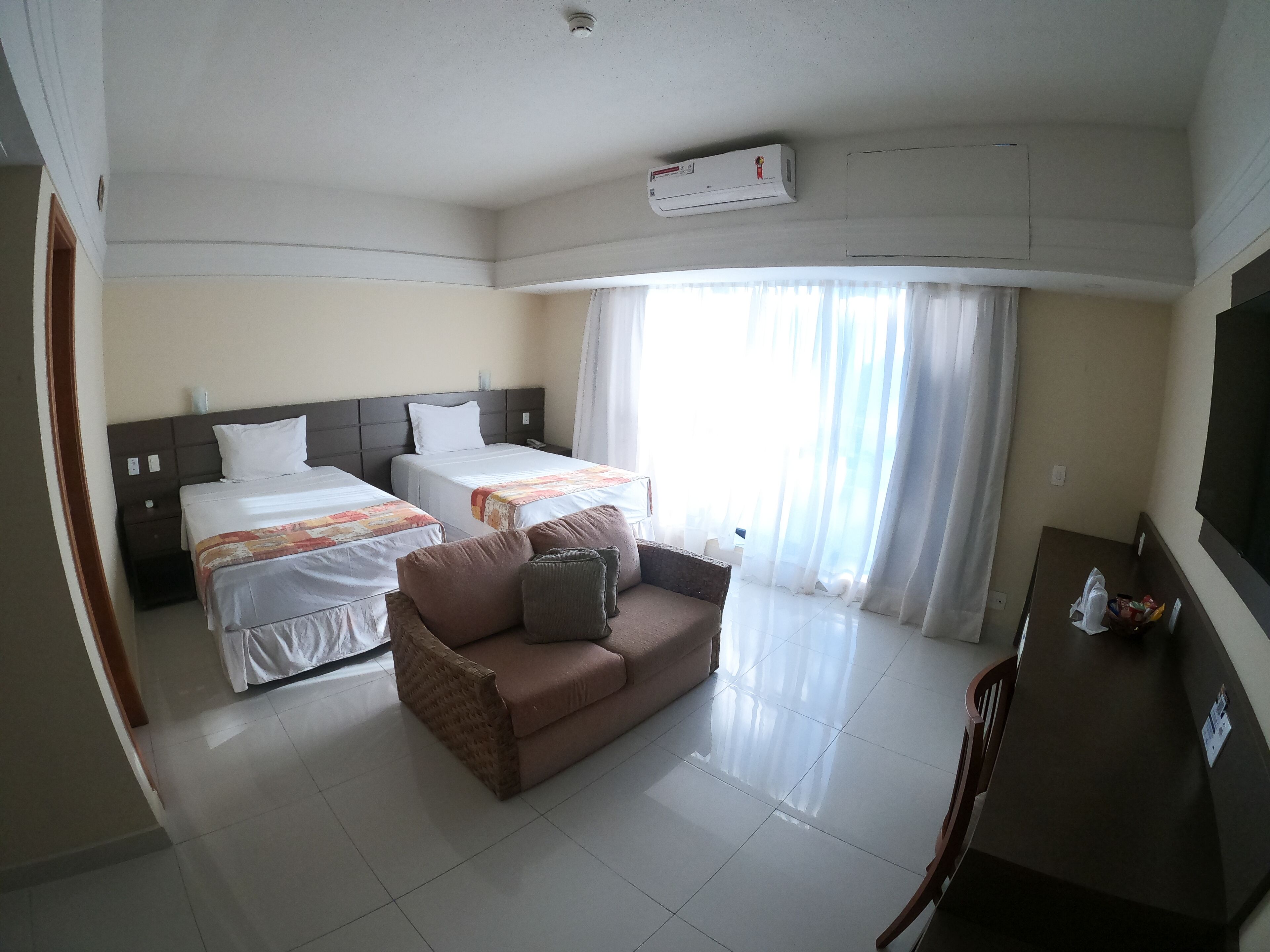 A hotel room with two beds, a sofa, a TV, and an air conditioning unit.