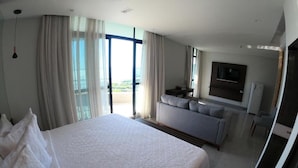 Habitación de hotel moderna con una cama grande, un sofá, un televisor y un balcón con cortinas.