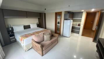 Quarto de hotel com cama, sofá, cozinha compacta e banheiro.