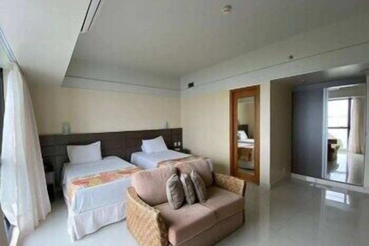 A hotel room with two beds, a sofa, a mirror, and a door leading to another room.