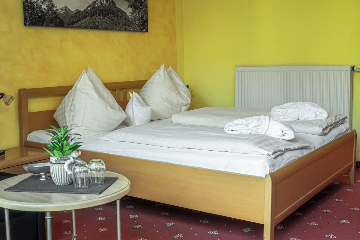 A hotel room with a wooden bed, white bedding, a small table with a plant, glasses, and a bowl.