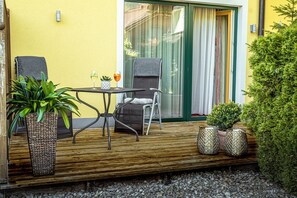 A wooden deck with a table and chairs, potted plants, and a sliding glass door leading to a room. - DAS Hintersee (Hintersee)