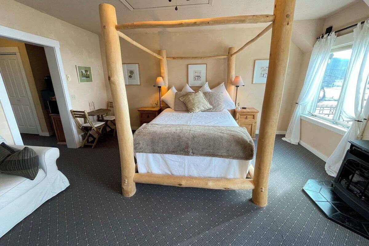 Una cama con dosel en una habitación con piso alfombrado, chimenea y ventana con cortinas.