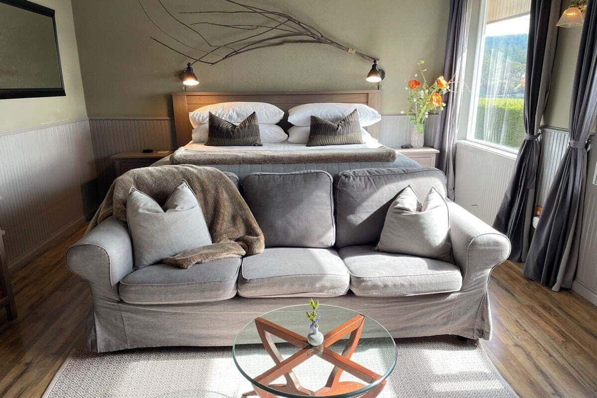 Una sala de estar moderna con un sofá gris, una mesa de centro de vidrio y una cama con cabecera de madera.