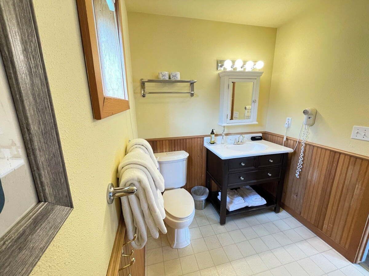 A bathroom with a toilet, sink, mirror, and towel rack.