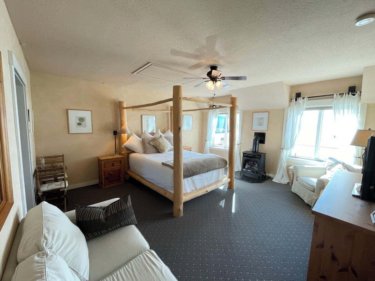 A bedroom with a four-poster bed, a desk, a chair, a small table, and a fireplace.
