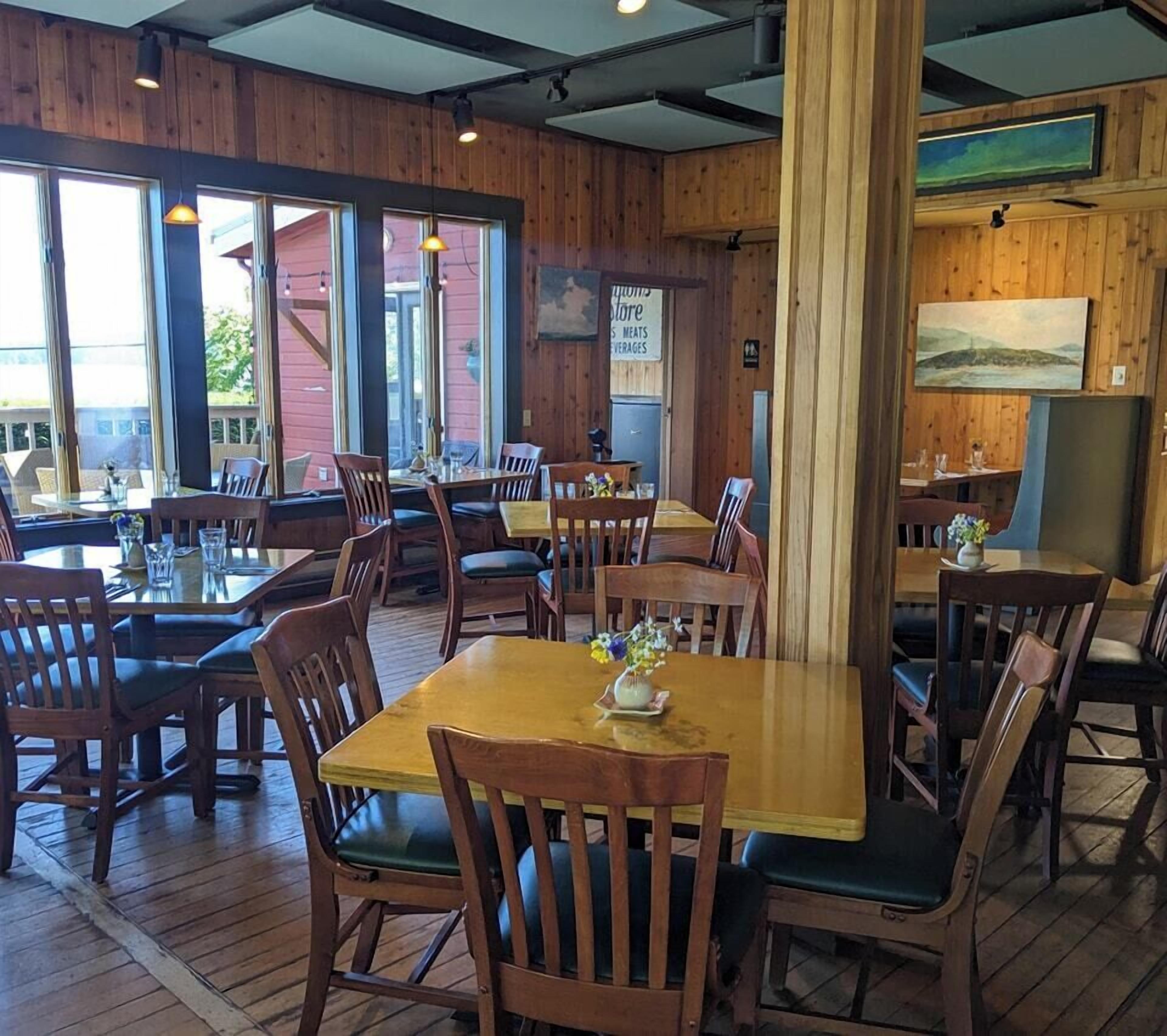 A restaurant with wooden interior, multiple tables and chairs, and large windows.