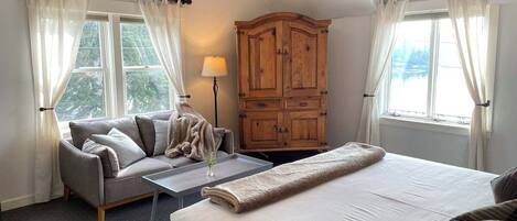 A bedroom with a bed, a sofa, a wooden wardrobe, a ceiling fan, and a window with curtains.