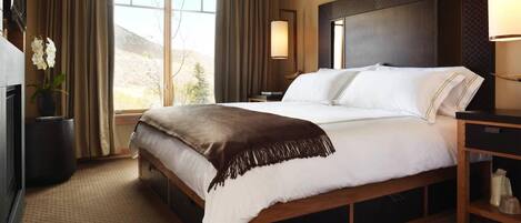 A hotel room with a large bed, a bedside table, a lamp, a TV, and a view of the outdoors.