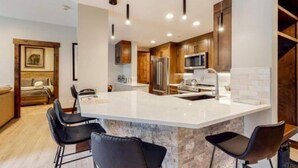 A modern kitchen with a large island, dark wooden cabinets, stainless steel appliances, and black bar stools. - Beaver Creek Charter 2 Bed (Avon)