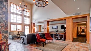 A spacious lobby with a stone accent wall, large windows, and a central seating area with red chairs. - 2 Bedroom Colorado Vacation Rental in River Run Village with Pool and Hot Tub Access (Keystone)