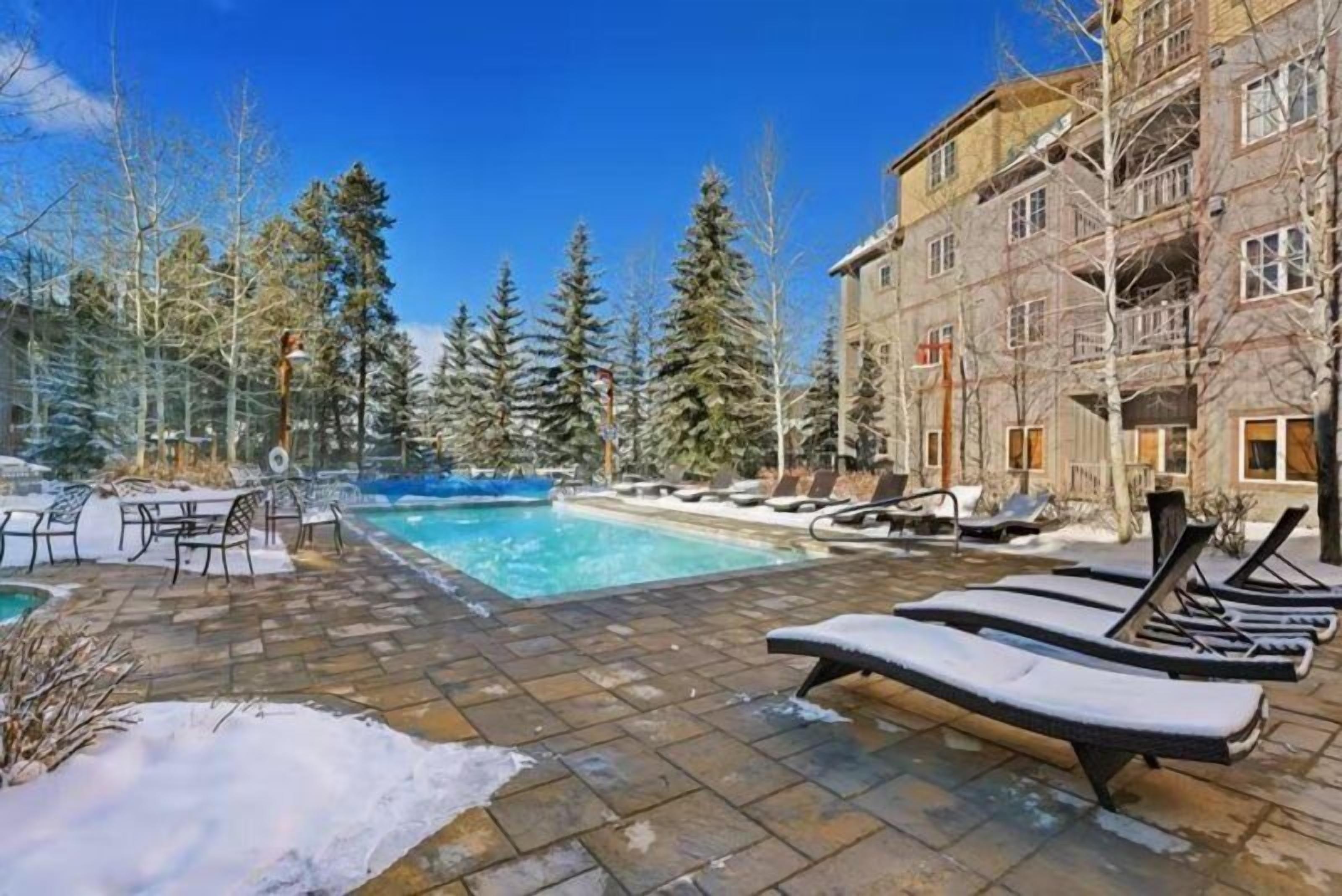 A pool area with lounge chairs and a building in the background. - 2 Bedroom Colorado Vacation Rental in River Run Village with Pool and Hot Tub Access (Keystone)