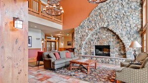 A spacious living area with a stone fireplace, a wooden ceiling, and a high ceiling balcony. - 2 Bedroom Colorado Vacation Rental in River Run Village with Pool and Hot Tub Access (Keystone)