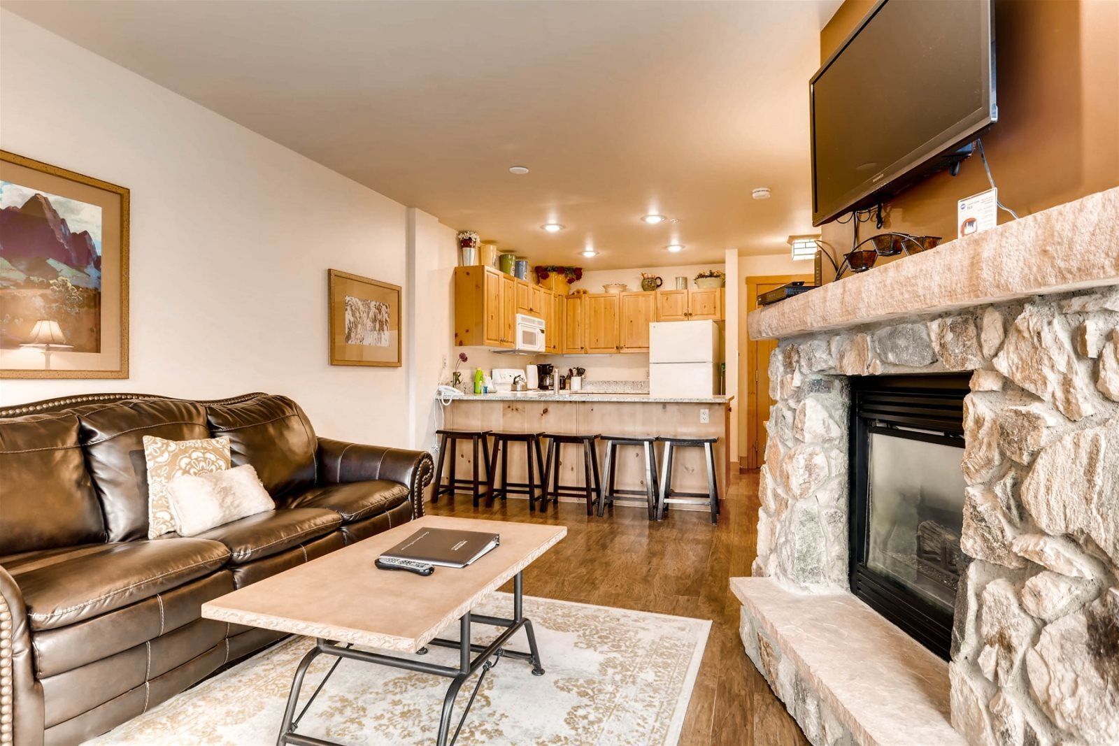A living room with a leather sofa, a coffee table, a fireplace, and a kitchen in the background.